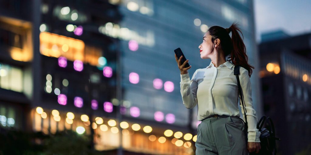A woman on a phone looks up at an office building at night.